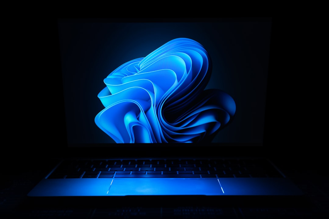A laptop displaying a stylized blue abstract design on its screen against a dark background.